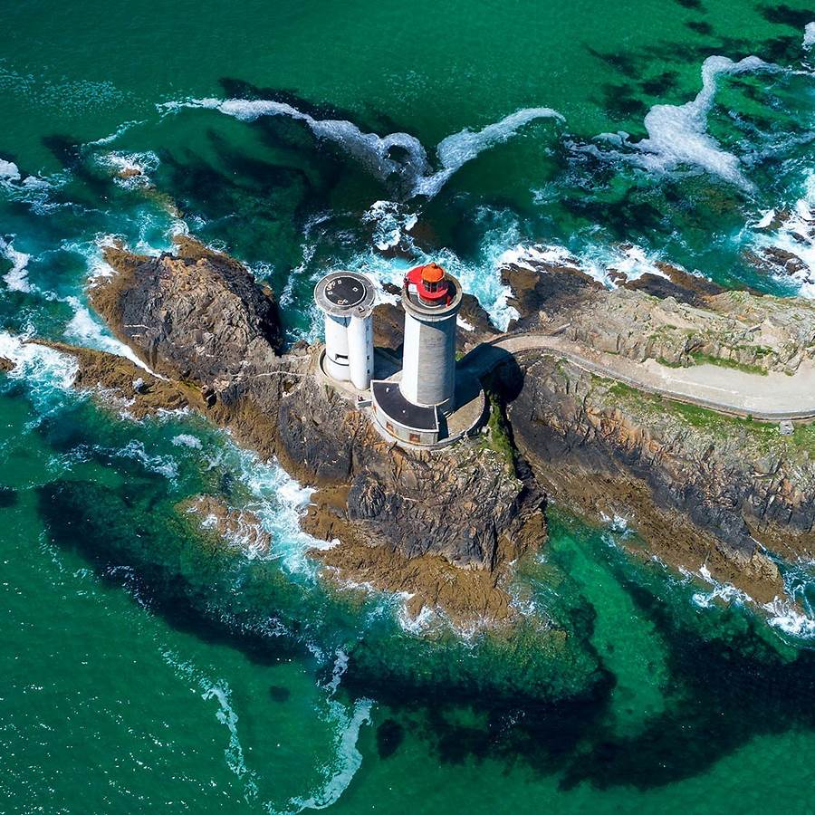 Aerial view of Petit Minou Lighthouse on rocky coast with turquoise sea and white surf