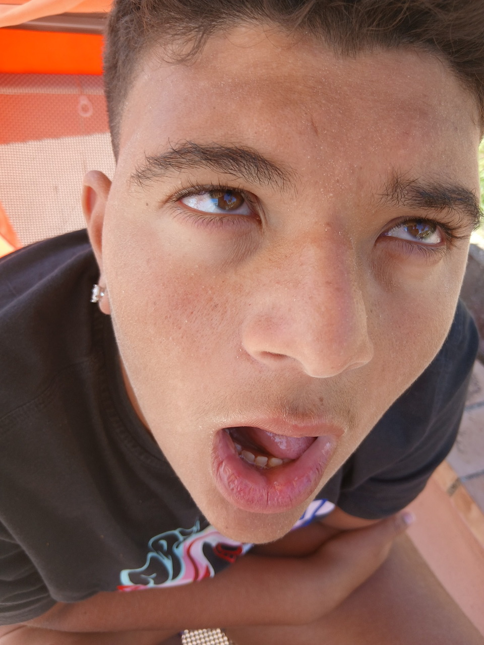 Close-up selfie of a young man with blue eyes, dark hair, and stud earring, mouth slightly open