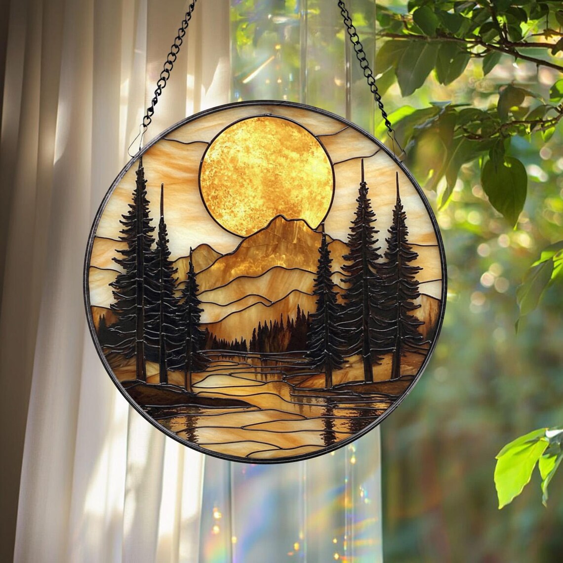 Round stained glass suncatcher with mountains, pine trees, and sun hanging by a window