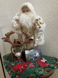 Santa Claus figurine in white robes with reindeer on rocking horse beside Christmas decorations