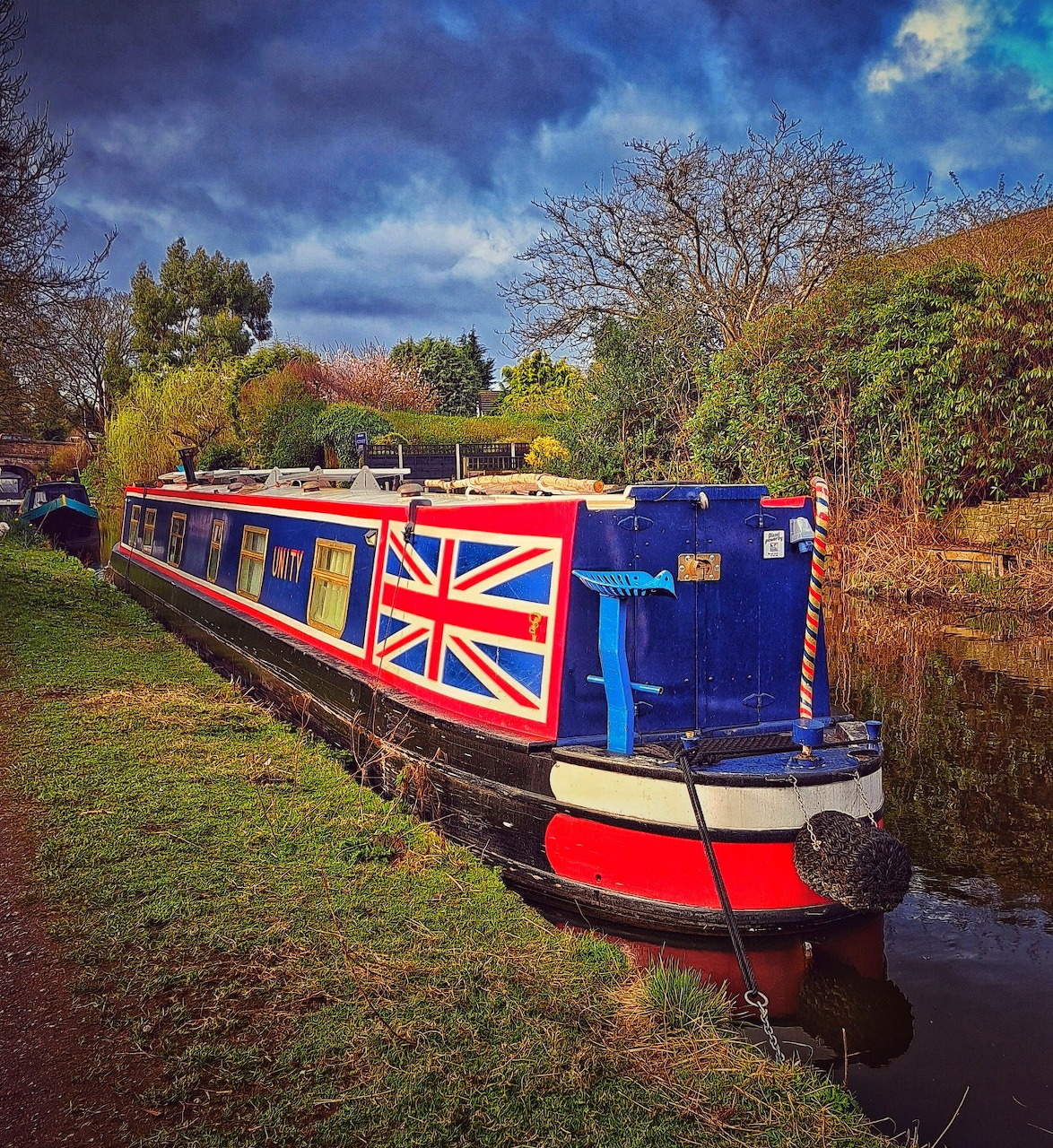 Union Jack narrowboat moored on a canal with trees and dramatic cloudy sky