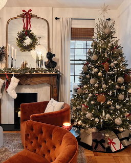 Living room with decorated Christmas tree, fireplace with wreath, and orange tufted armchair