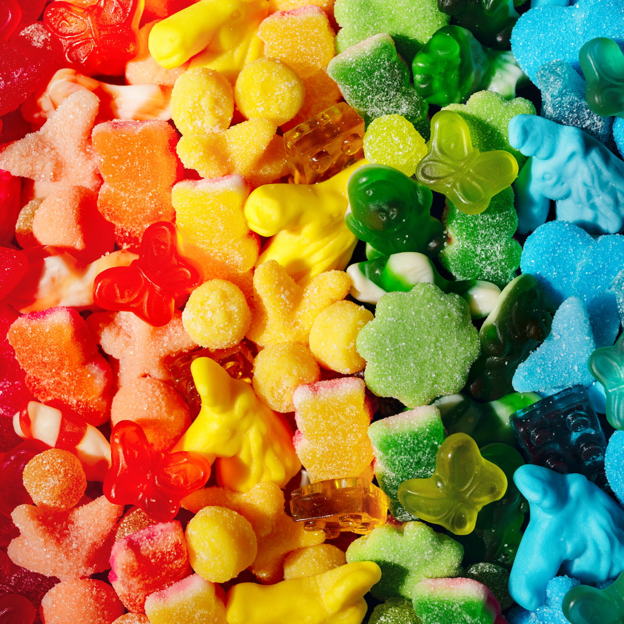 Rainbow gradient of gummy bears and candies in red, yellow, green, and blue colors arranged in diagonal rows