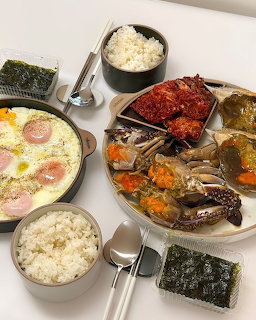Tabletop meal with marinated crabs, rice bowls, seaweed, and a creamy egg dish with sausage slices