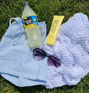 Overhead view of summer accessories including sunglasses, drink bottle, sunscreen and towels arranged on green grass