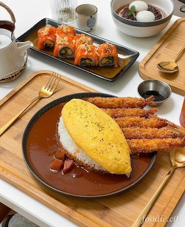 Plate of curry rice topped with breaded pork cutlet and Korean side dishes on wooden table