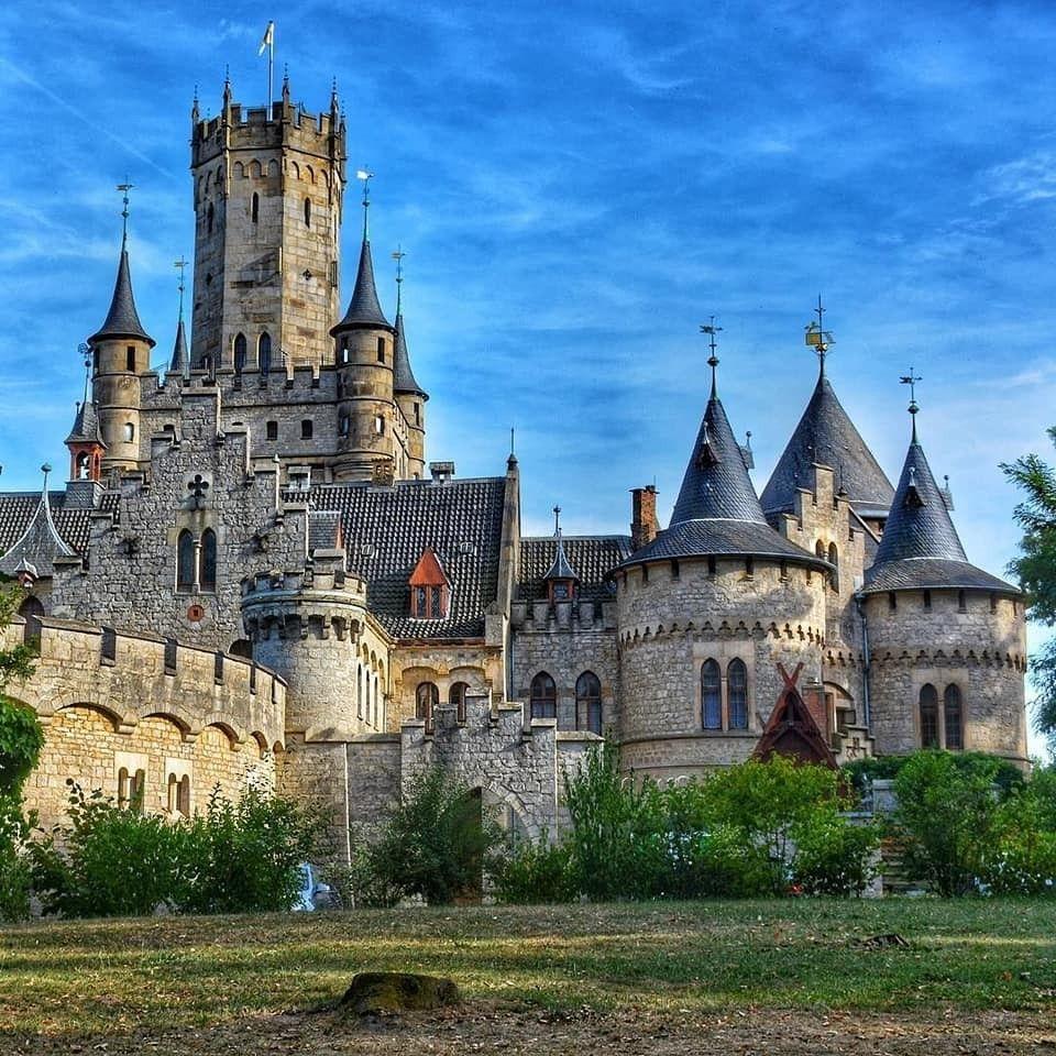 Stone castle with tall central tower and round turrets beneath a blue sky
