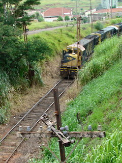 Freight train on tracks through green rural hillside with buildings in distance