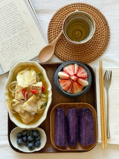 Wooden tray with purple sweet potatoes, soup, strawberries, blueberries, tea cup, and an open book