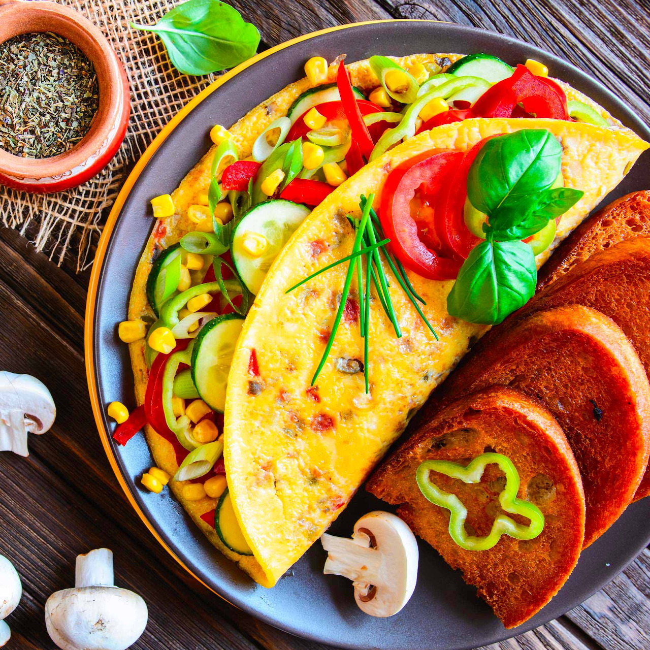 Omelette with vegetables, tomatoes, toast, and basil on a blue plate with wooden background