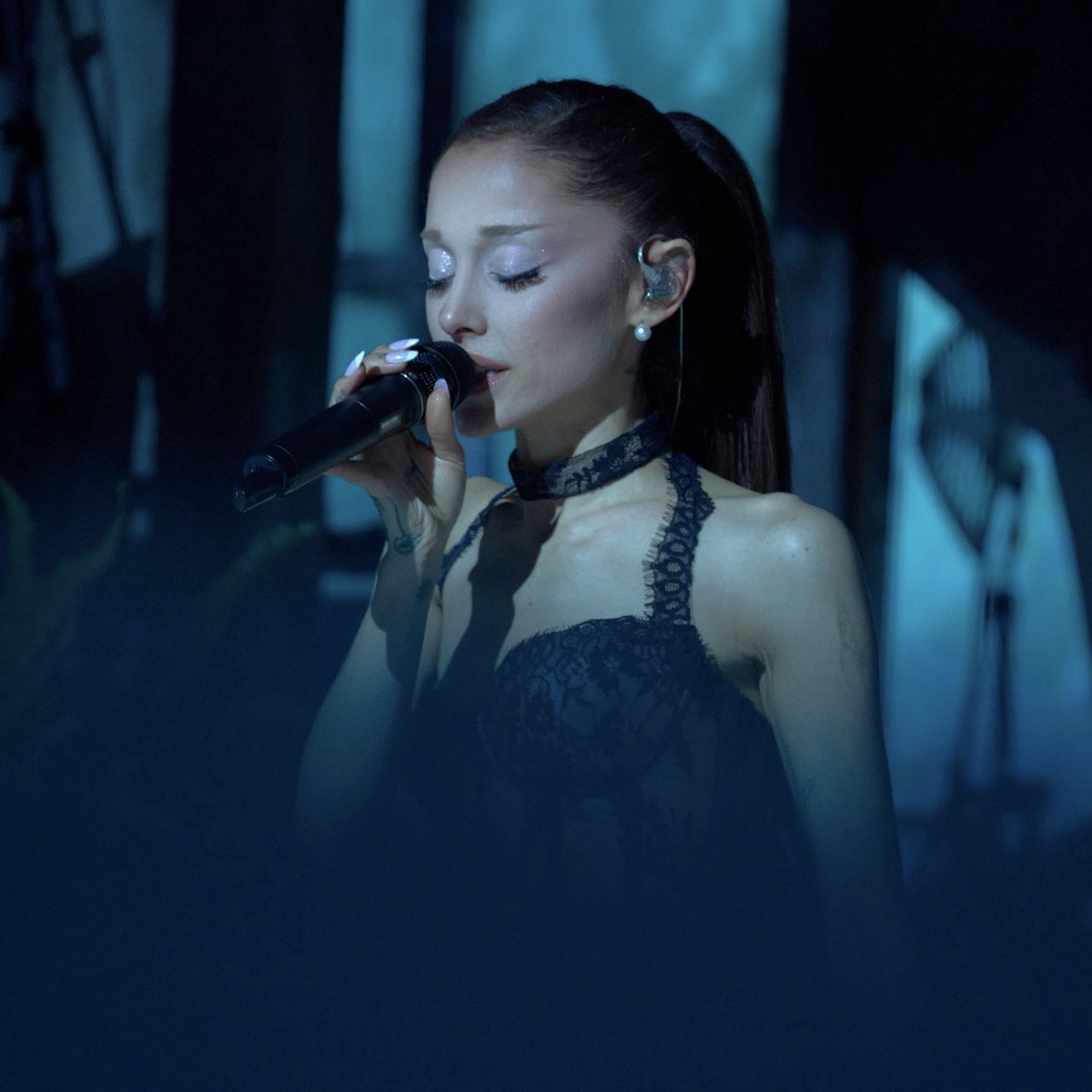 Ariana Grande singing into a microphone on a dark stage