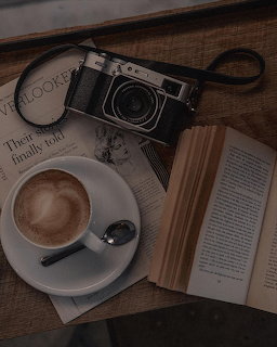 Cup of latte with heart art, vintage camera, open book, and magazine on a wooden table