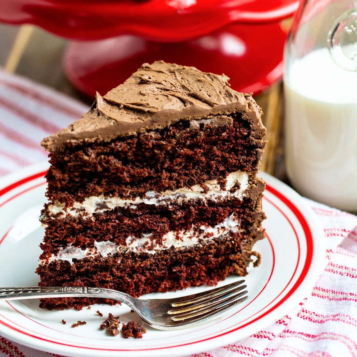 Slice of layered chocolate cake with white cream filling and chocolate frosting on red-trimmed plate