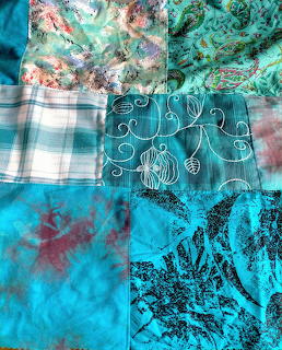 Turquoise patchwork quilt with floral, tie-dye, and plaid fabric squares arranged in a grid pattern
