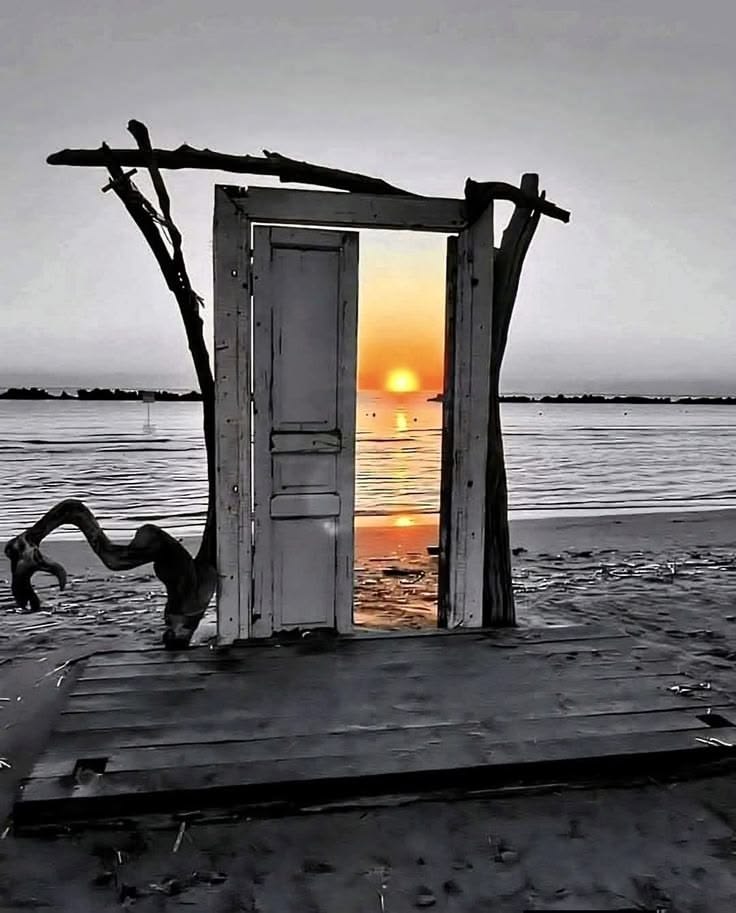 Weathered door frame on a beach with an orange sunrise visible through the doorway