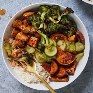 White bowl with chicken, broccoli, cucumbers, sweet potatoes, and rice with a gold fork
