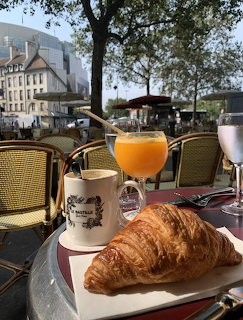 Croissant, orange juice, and coffee on outdoor café table with wicker chairs