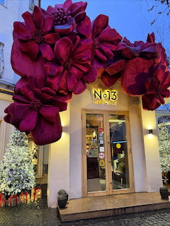 Storefront with massive dark red decorative flowers arching over the entrance at evening time