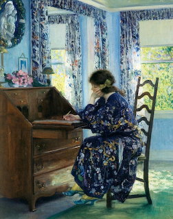 Woman in blue floral robe writing at wooden desk near window with decorative curtains