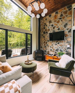 Modern living room with decorative stone wall, large windows, white sofa, green chairs, and wood ceiling