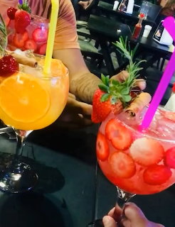 Three colorful fruit cocktails in large glasses with strawberry and orange garnishes and colorful straws