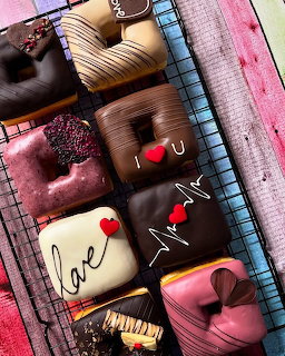 Assorted decorated chocolate truffles and bonbons on a wire rack over a pink wooden surface.