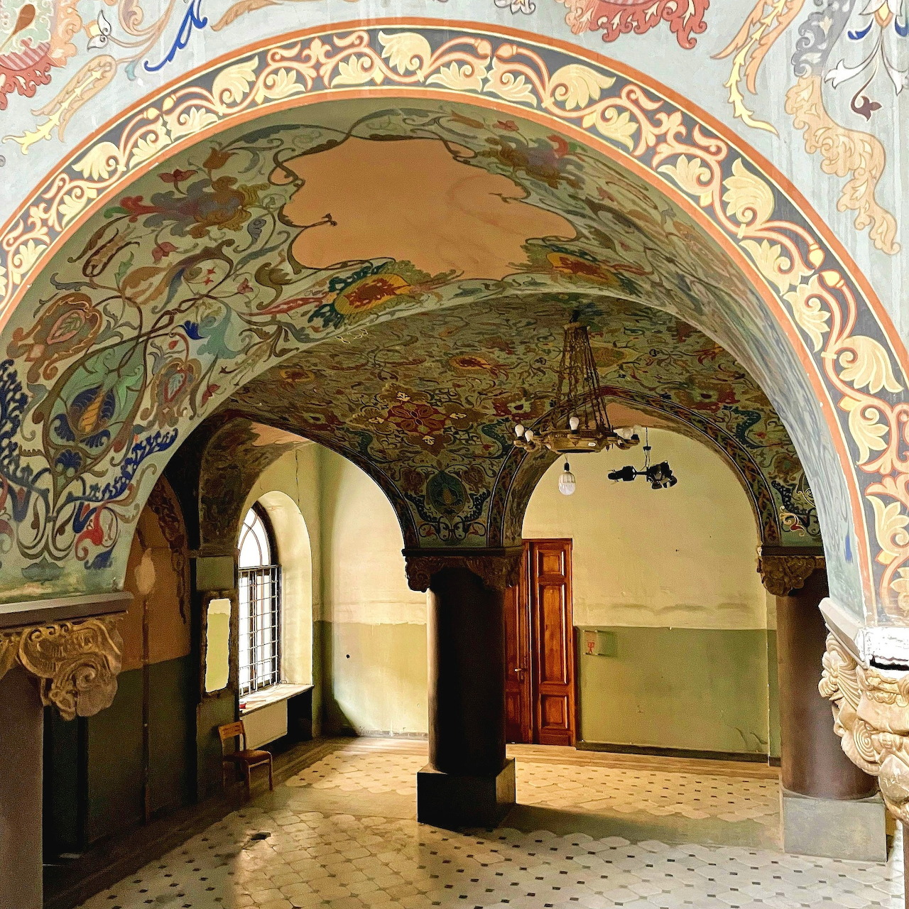 Historic interior with ornate painted arches, columns, tiled floor, and open wooden doors