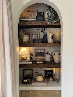 Arched built-in shelving unit with rustic wood shelves decorated with candles, vases, plants, and books