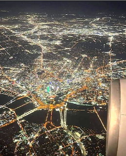 Aerial view of illuminated city at night with bridges and streets glowing, airplane wing visible in corner