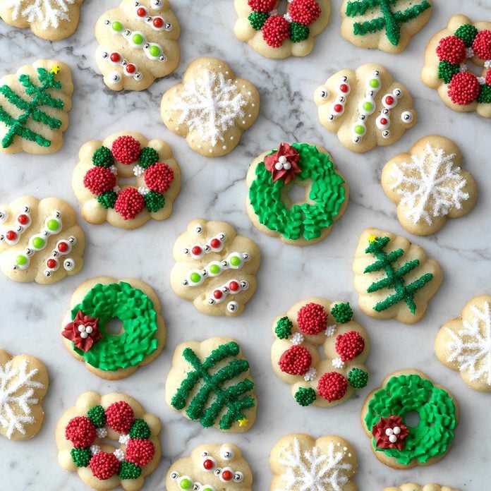 Assorted Christmas spritz cookies with green, white, and red frosting in holiday shapes on marble background