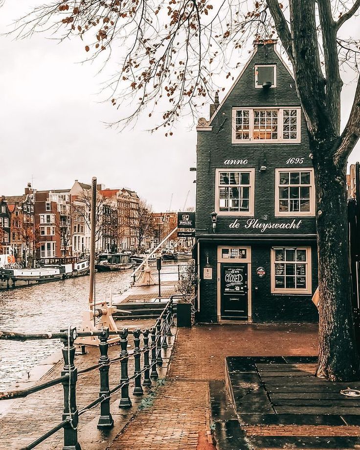 Traditional Dutch canal house with distinctive architecture beside an Amsterdam waterway on an overcast day