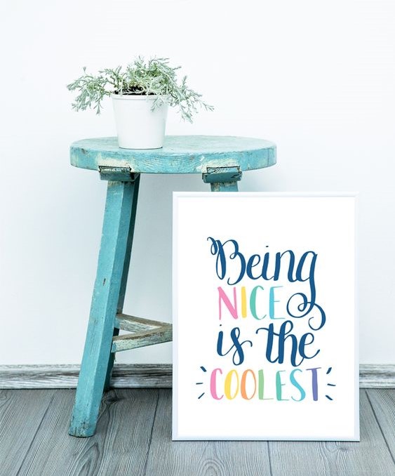 Hand-lettered 'Being Nice is the Coolest' sign in rainbow colors beside turquoise stool with succulent