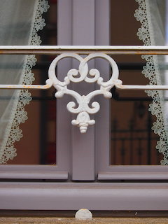 Close-up of a gray window with lace curtains and decorative white metal railing
