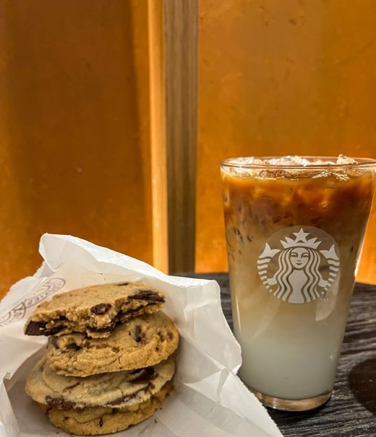 Iced coffee in a glass next to stacked chocolate chip cookies on a table