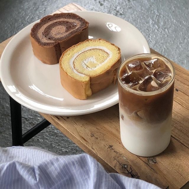 Layered iced coffee with ice beside two Swiss roll cake slices on a white plate