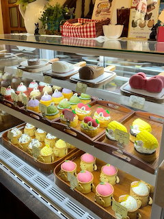 Glass bakery display case filled with colorful pastries, cakes, and desserts on wooden trays