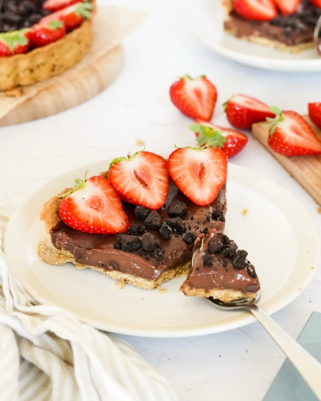 Slice of chocolate tart with sliced strawberries and chocolate chips on a white plate