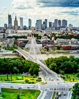 Warsaw skyline with a cable-stayed bridge over the river and green trees in the foreground