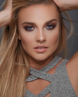 Close-up portrait of a blonde woman with smoky eye makeup and long hair wearing a gray cutout top