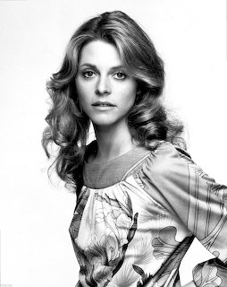 Black and white portrait of a woman with curly hair wearing a floral blouse, 1970s style