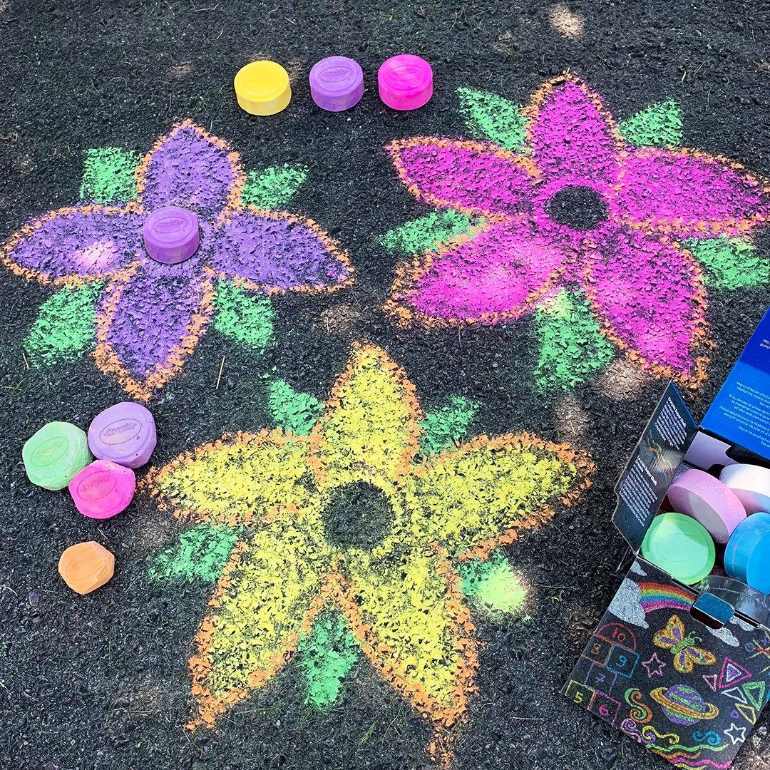 Three large colorful chalk flowers drawn on pavement with chalk pieces nearby