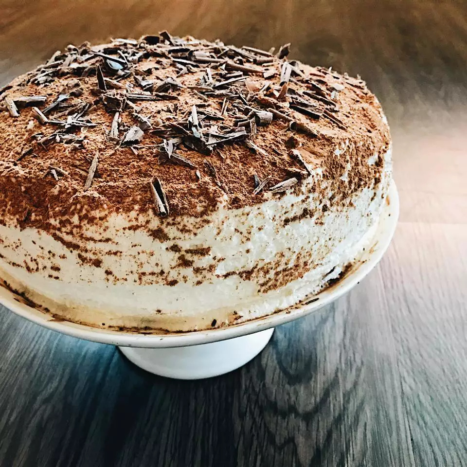 Tiramisu layer cake with cocoa dusting and chocolate shavings on white cake stand