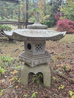 Traditional Japanese stone lantern in a garden with autumn trees and green grass