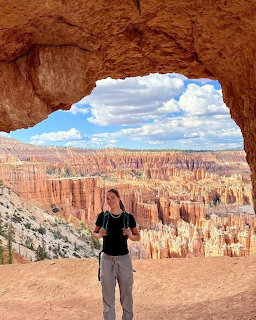 Person standing under a natural rock arch with Bryce Canyon hoodoos visible in the background