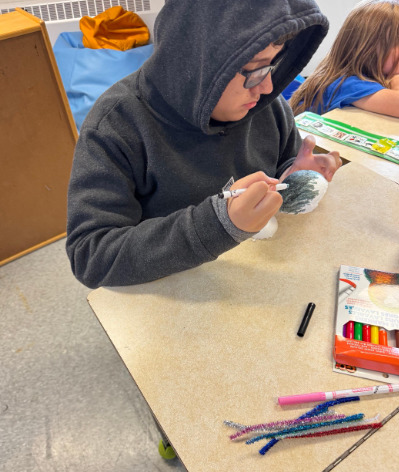 Student in gray hoodie drawing with markers at classroom desk