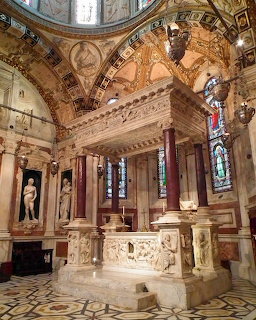 Ornate baroque chapel interior with domed ceiling, marble altar, columns, and stained glass windows in warm lighting