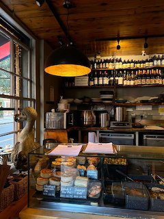 Cozy cafe interior with pastry display case, hanging lamp, shelves of bottles, and window