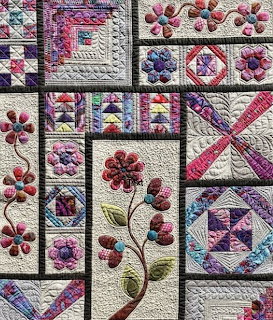 Colorful patchwork quilt with floral appliqué and geometric block patterns in pink and purple tones