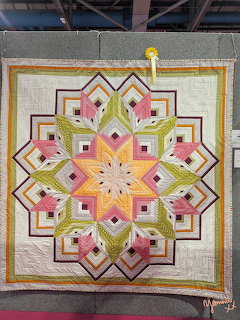 Handmade quilt with geometric star pattern in pink, green, yellow, and orange displayed at a quilt show