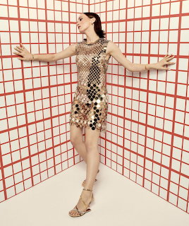 Woman in gold sequin dress dancing against red grid wall